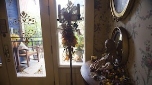 A room with a door leading to a balcony, a mirror on the wall, and a decorative plant arrangement.