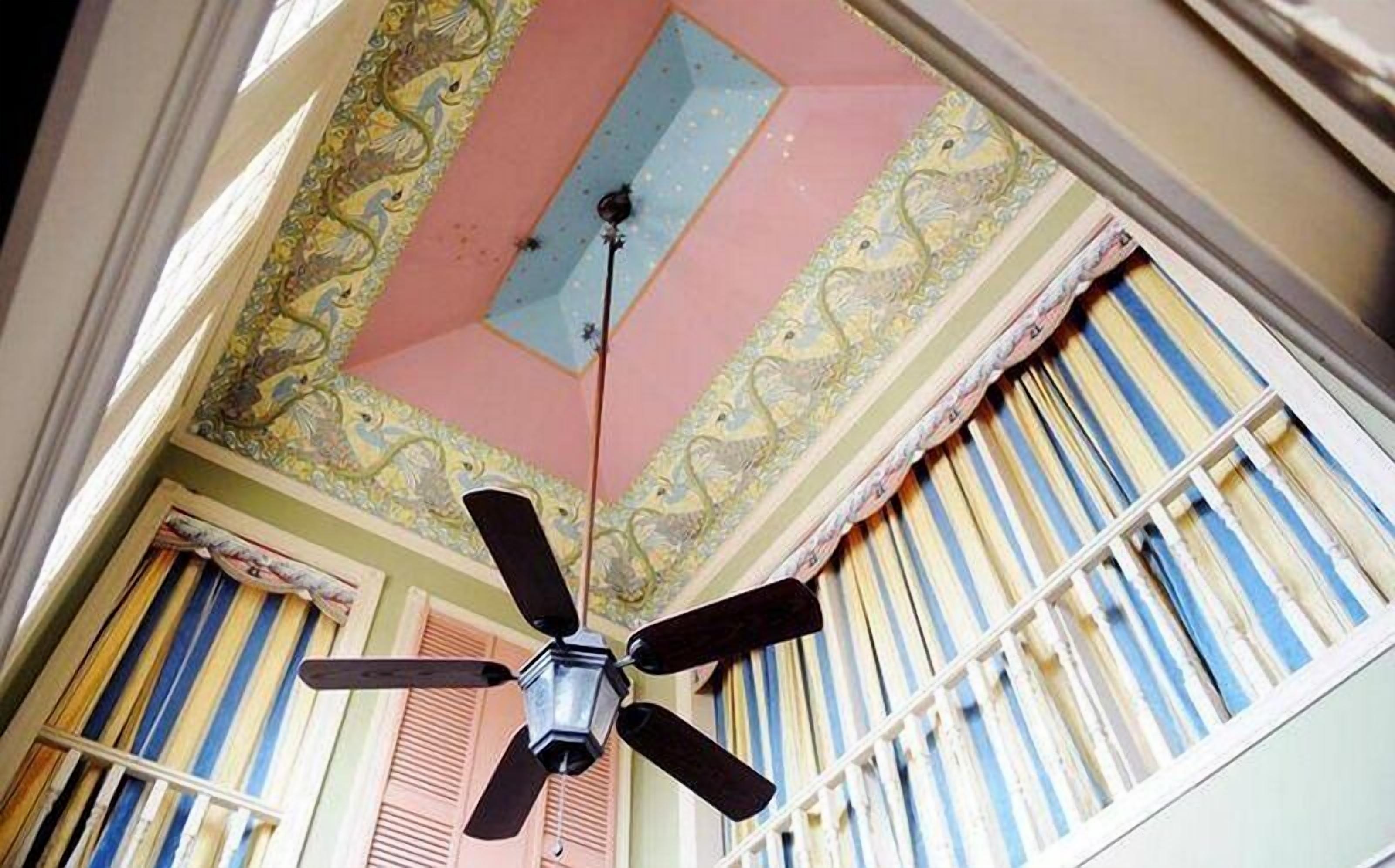 A ceiling fan in a room with striped window shutters and ornate ceiling decorations.