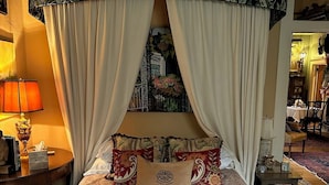 A hotel room with a large bed, a canopy, and a view of a balcony with flowers.