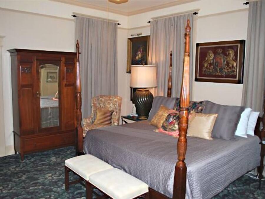 Un dormitorio con una cama con dosel, un armario de madera, una silla y una lámpara.