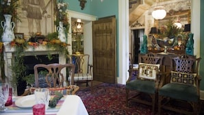 A dining area with a table set for a meal, chairs, a fireplace, and a large painting on the wall.