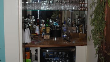 Un coin bar avec des étagères remplies de verres et de bouteilles, un réfrigérateur contenant des boissons et une chaise en bois.