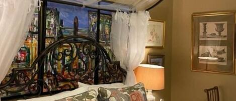 Een bed met hemelbed, bloemenbeddengoed en een schilderij aan de muur.
