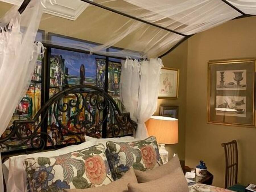 A bed with a canopy, floral bedding, and a painting on the wall.