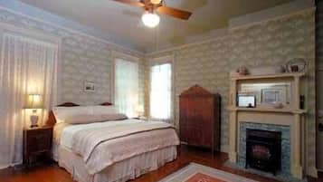 A bedroom with a bed, a nightstand, a wooden wardrobe, a fireplace, and a ceiling fan.
