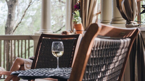 A wooden chair with a woven backrest and a glass of white wine on a table. - Princess Anne Boutique Hotel (Asheville)