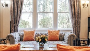 A cozy seating area with a sofa and a table, a window with curtains, and a vase with flowers. - Princess Anne Boutique Hotel (Asheville)