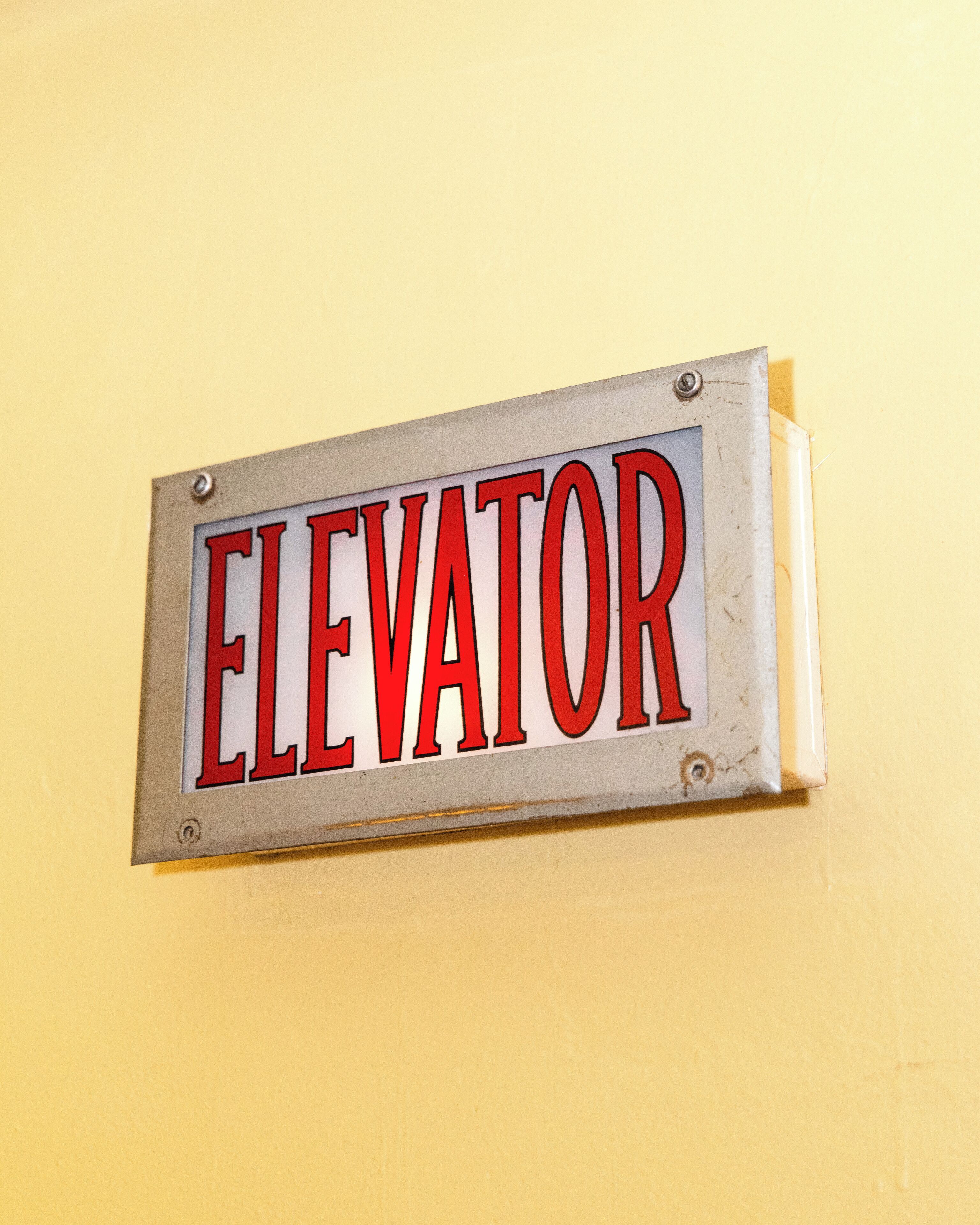 A sign with the word "ELEVATOR" mounted on a yellow wall.