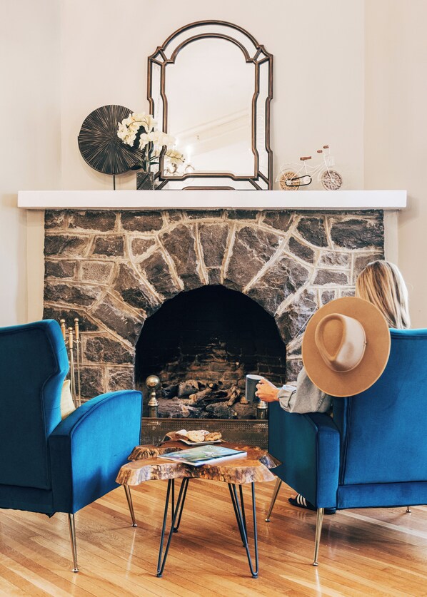 A room with a stone fireplace, two blue armchairs, a coffee table, and a person holding a mug. - Princess Anne Boutique Hotel (Asheville)