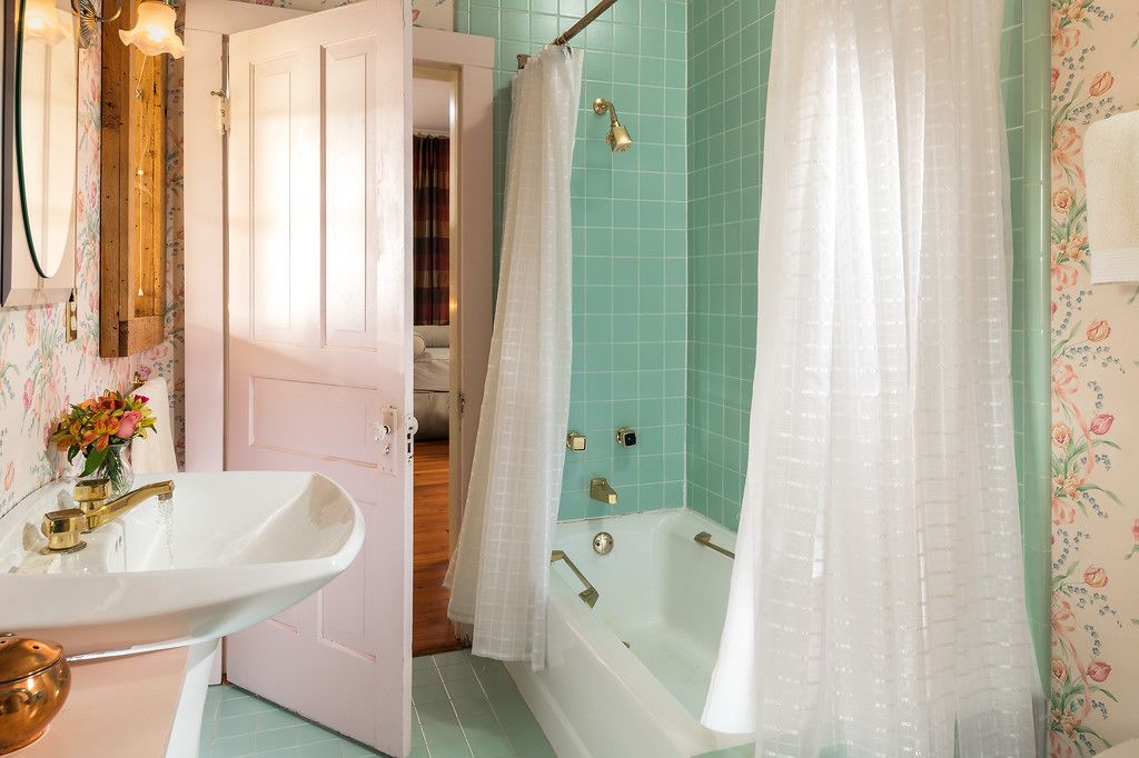 Un baño con un lavabo blanco, una bañera con cortina de ducha y una puerta que da a otra habitación.