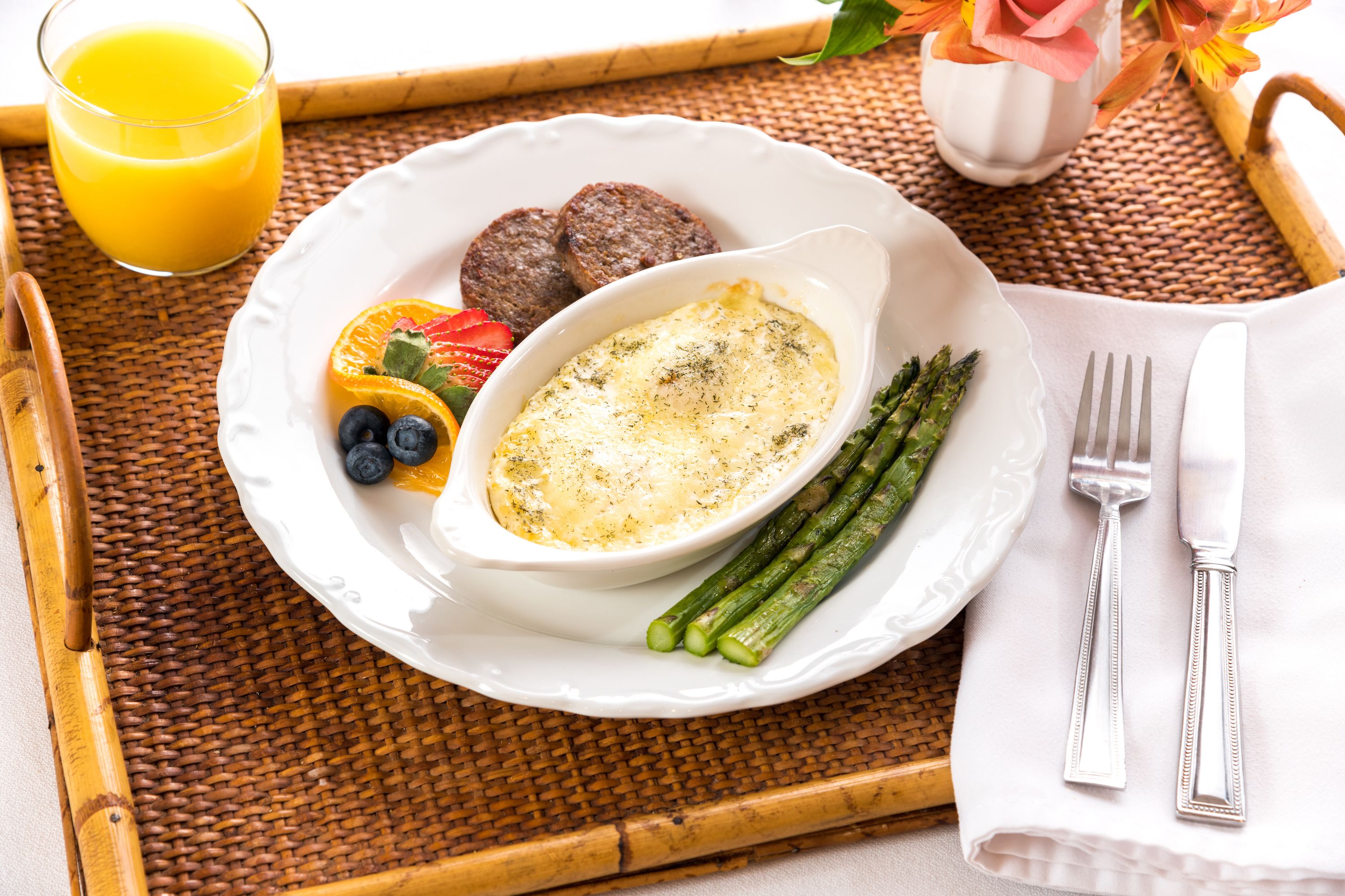 A breakfast tray with a plate of food, including eggs, asparagus, and berries, and a glass of orange juice.