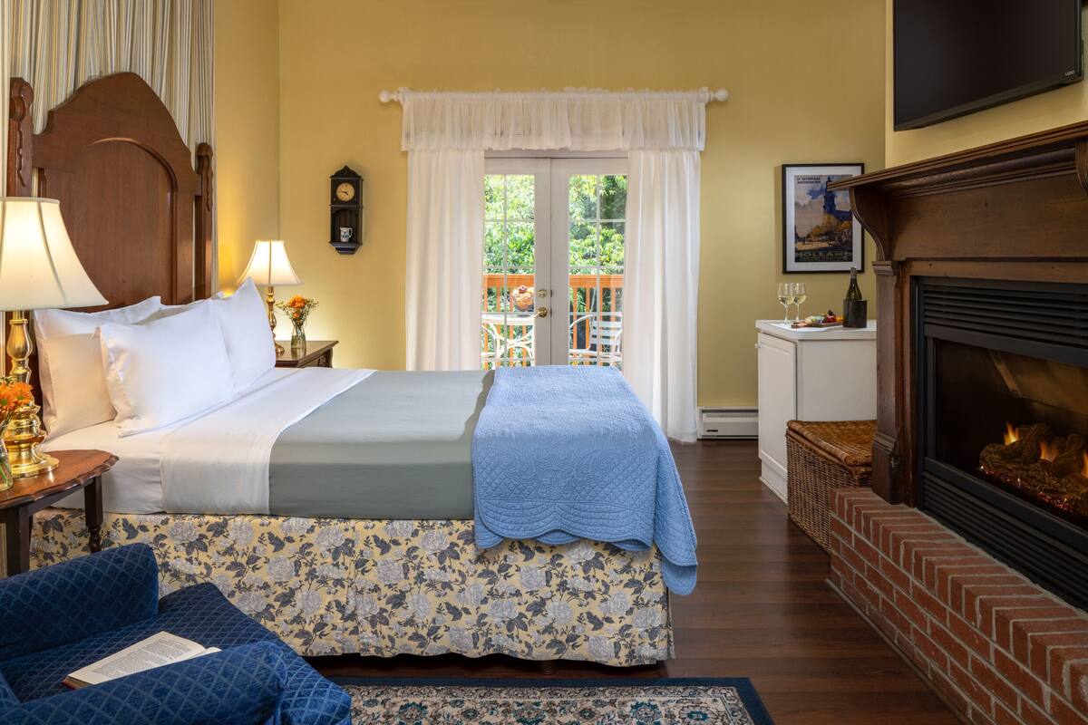 A hotel room with a bed, a fireplace, a balcony with a view, and a dining area with a table and chairs.