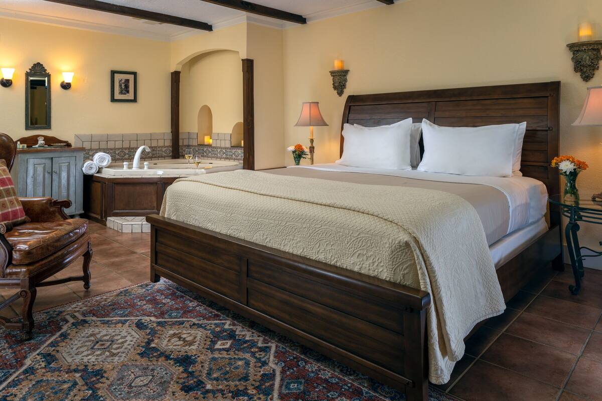 A bedroom with a large bed, a wooden nightstand, a dresser, and a bathroom with a sink and mirror.