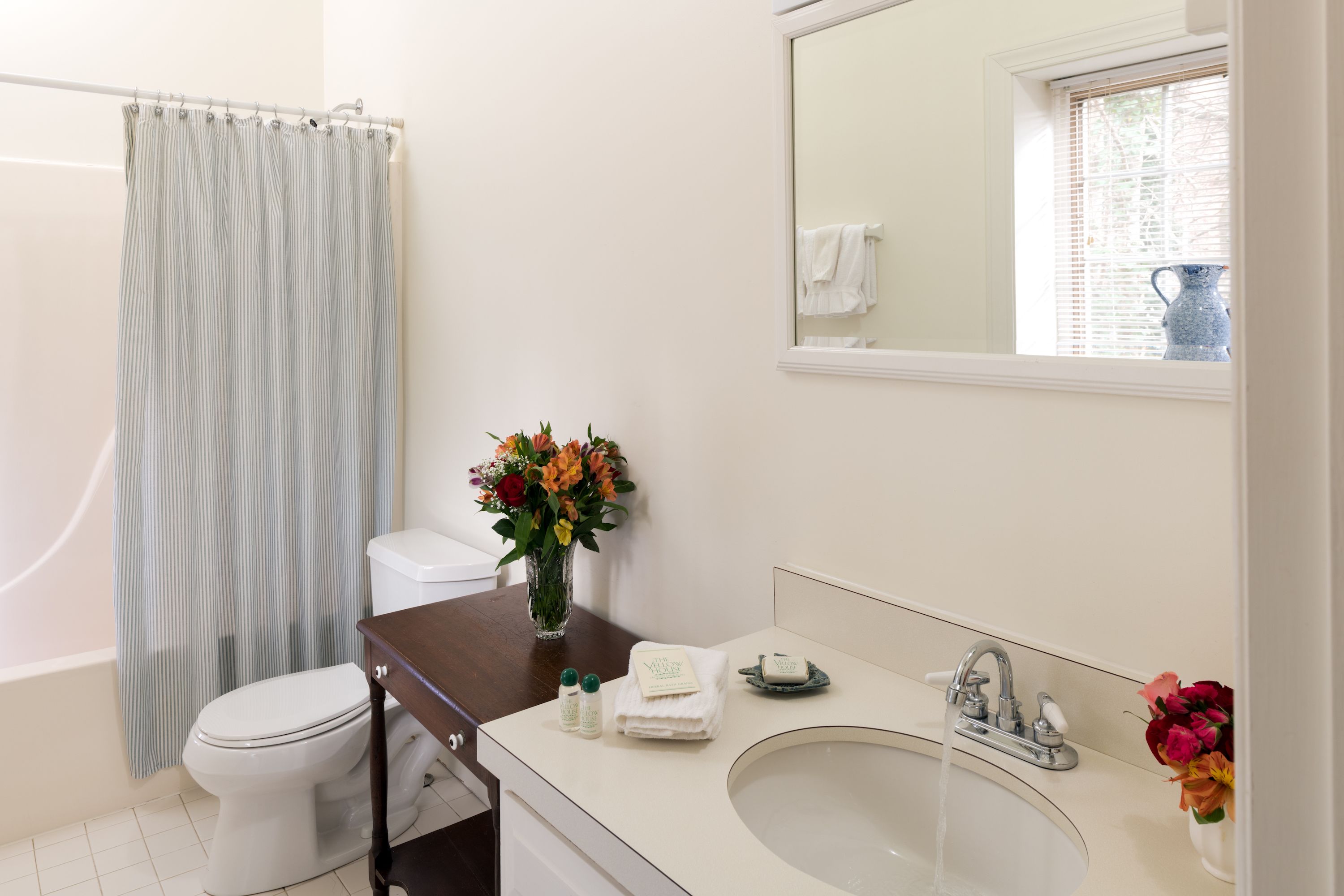 A bathroom with a toilet, a sink, a shower curtain, and a vase of flowers.