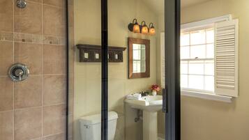 A bathroom with a shower, toilet, sink, and a window with shutters.