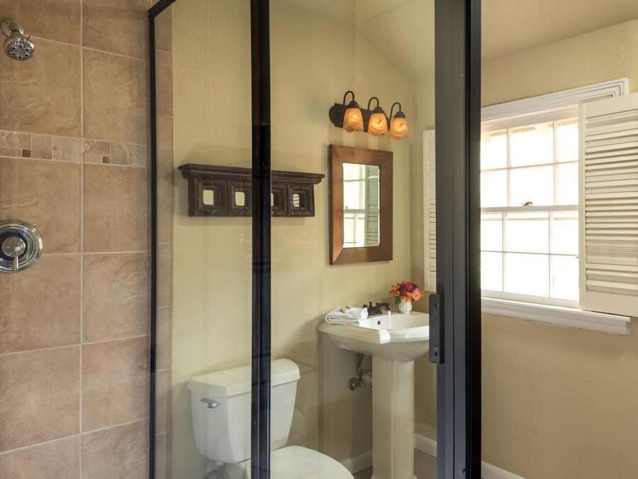A bathroom with a shower, toilet, sink, and a window with shutters.