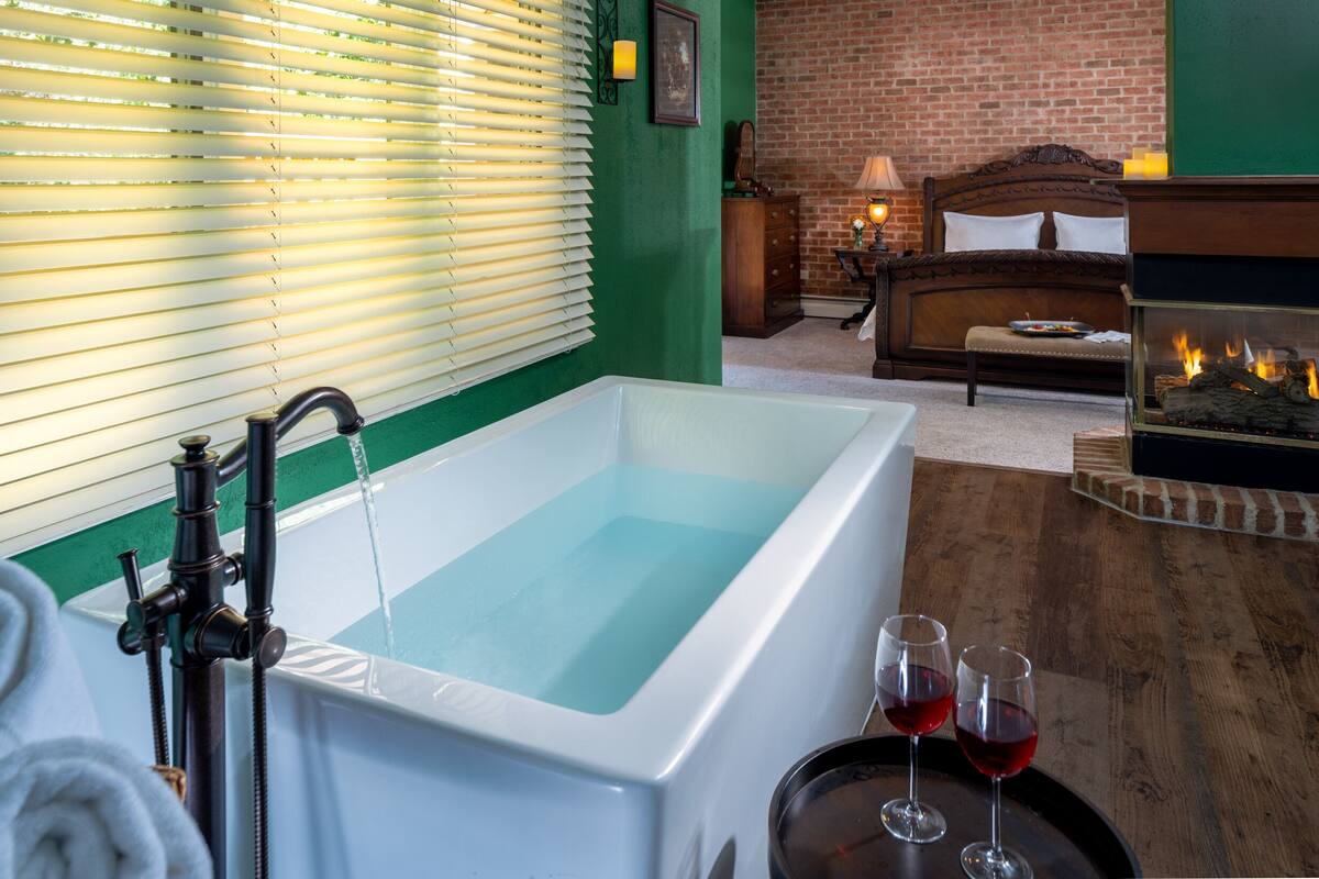 A modern bathroom with a bathtub, a wooden bench, and a fireplace.
