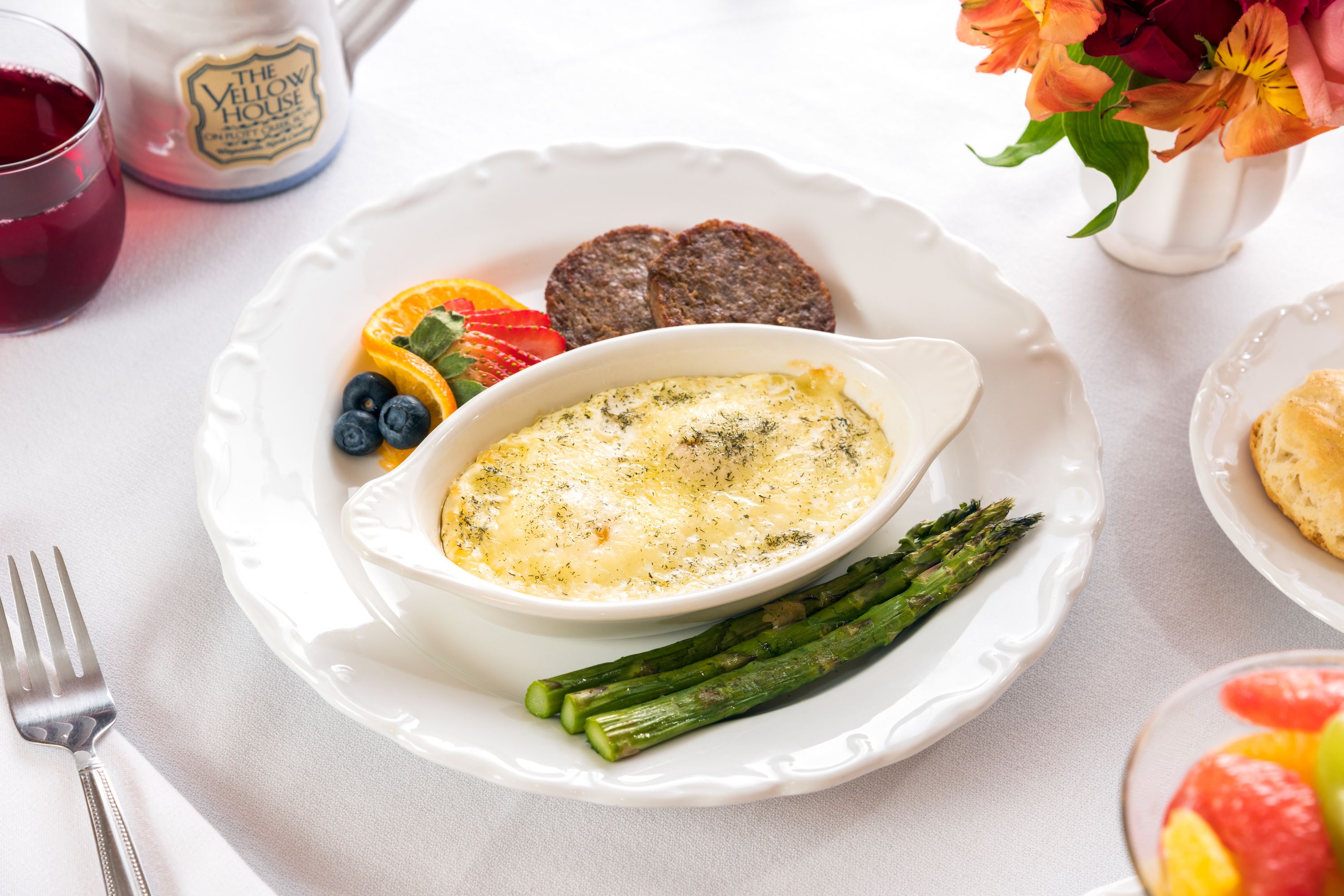 A breakfast plate with eggs, asparagus, and berries, a mug, and a vase with flowers.
