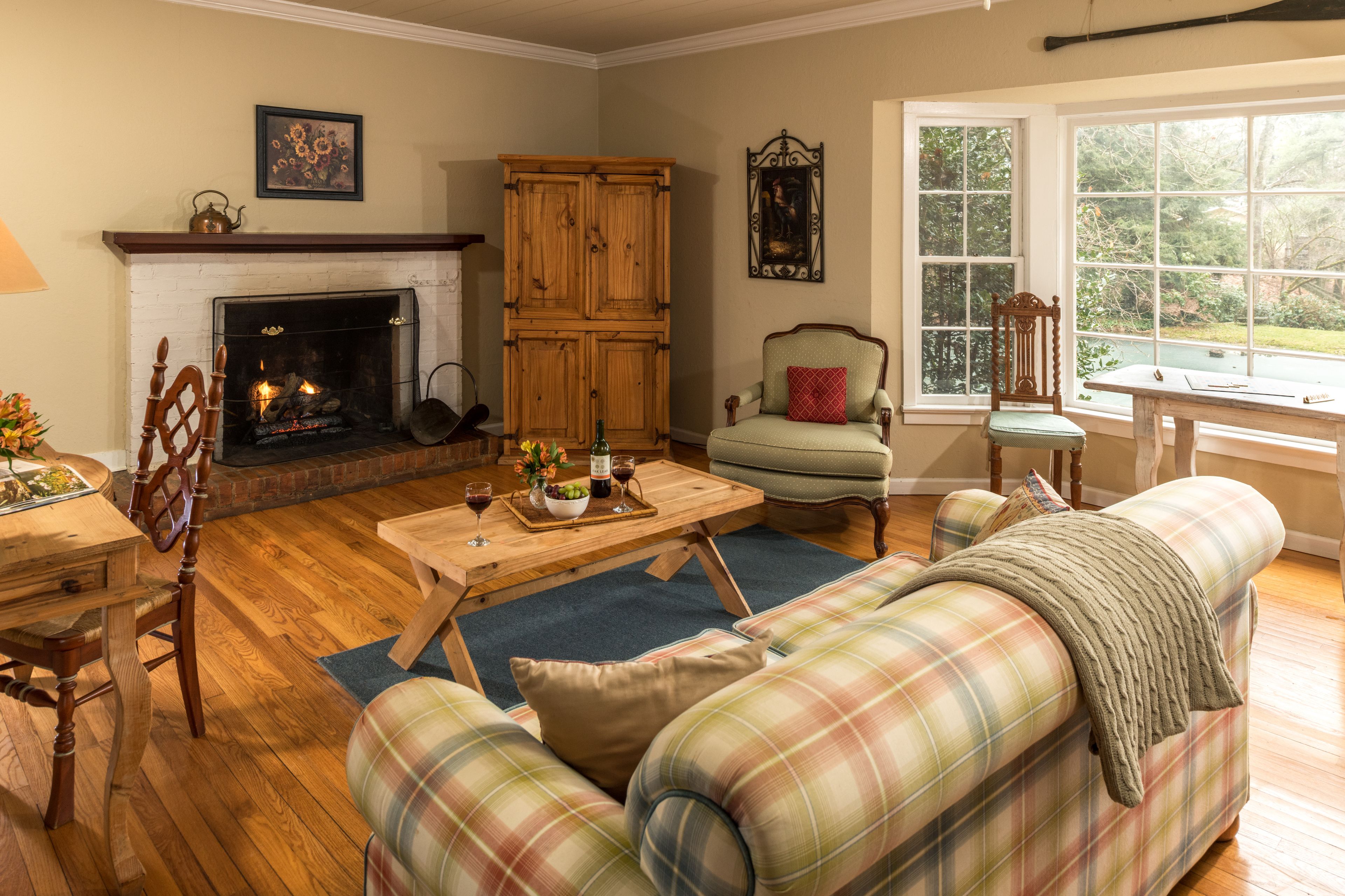 Un salon chaleureux avec une cheminée, des meubles en bois et une vue dégagée sur l’extérieur grâce à une grande fenêtre.