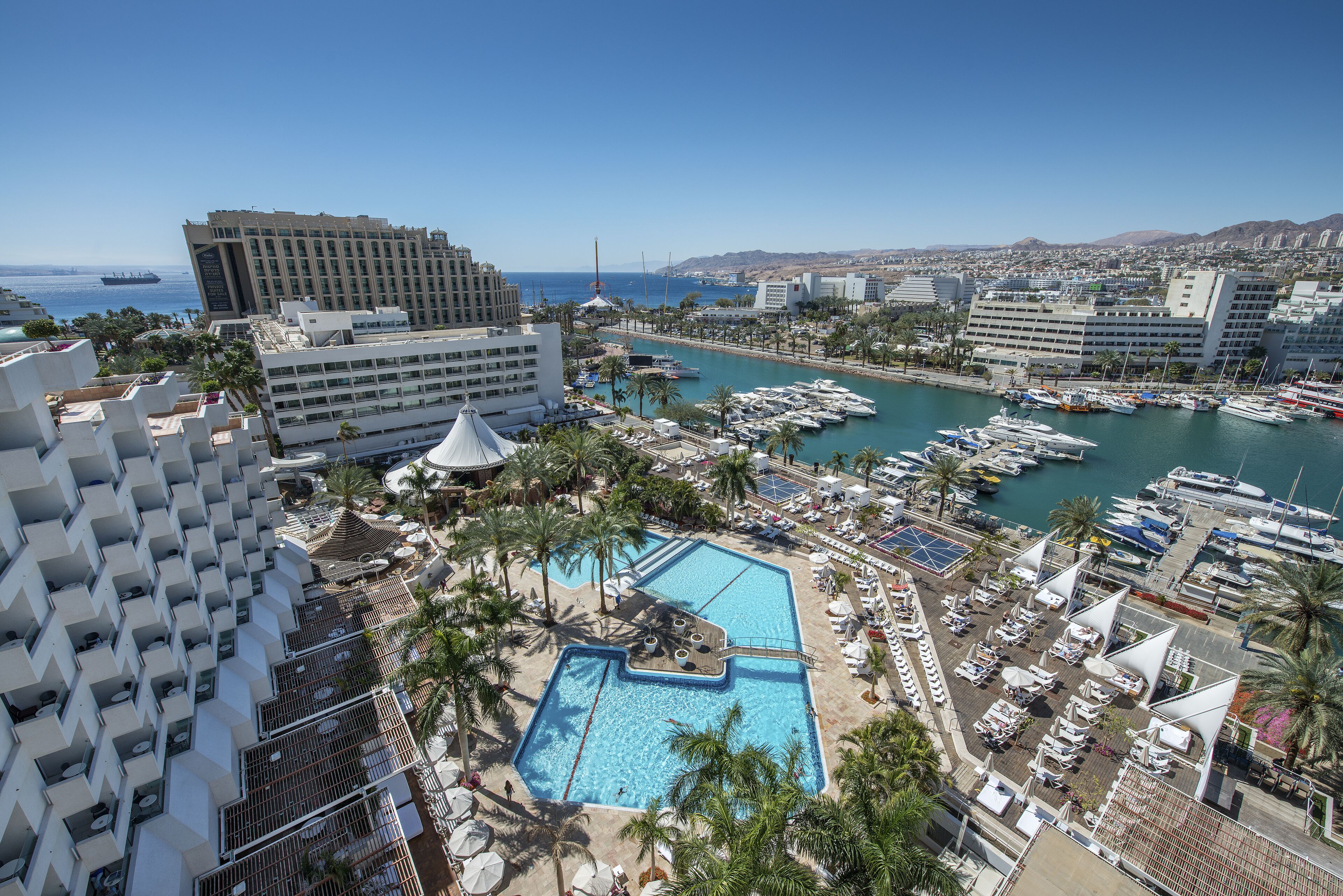 A resort with a large swimming pool, multiple buildings, and a marina with boats.