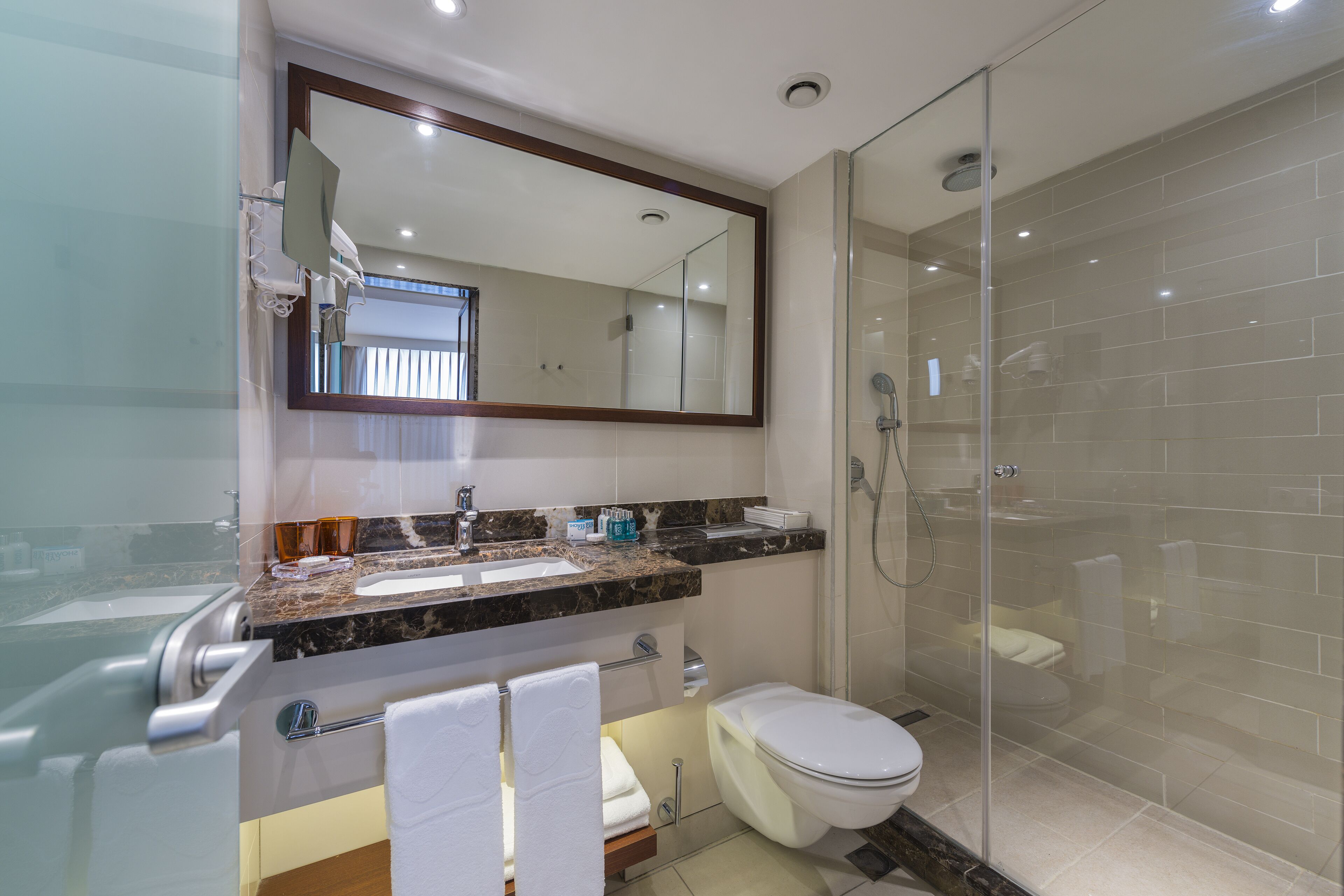 A modern bathroom with a glass-enclosed shower, a marble countertop, and a large mirror.