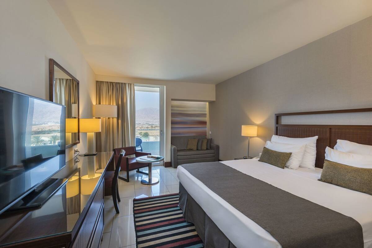 Quarto de hotel com cama, televisão, escrivaninha, cadeira, sofá e vista para a cidade.