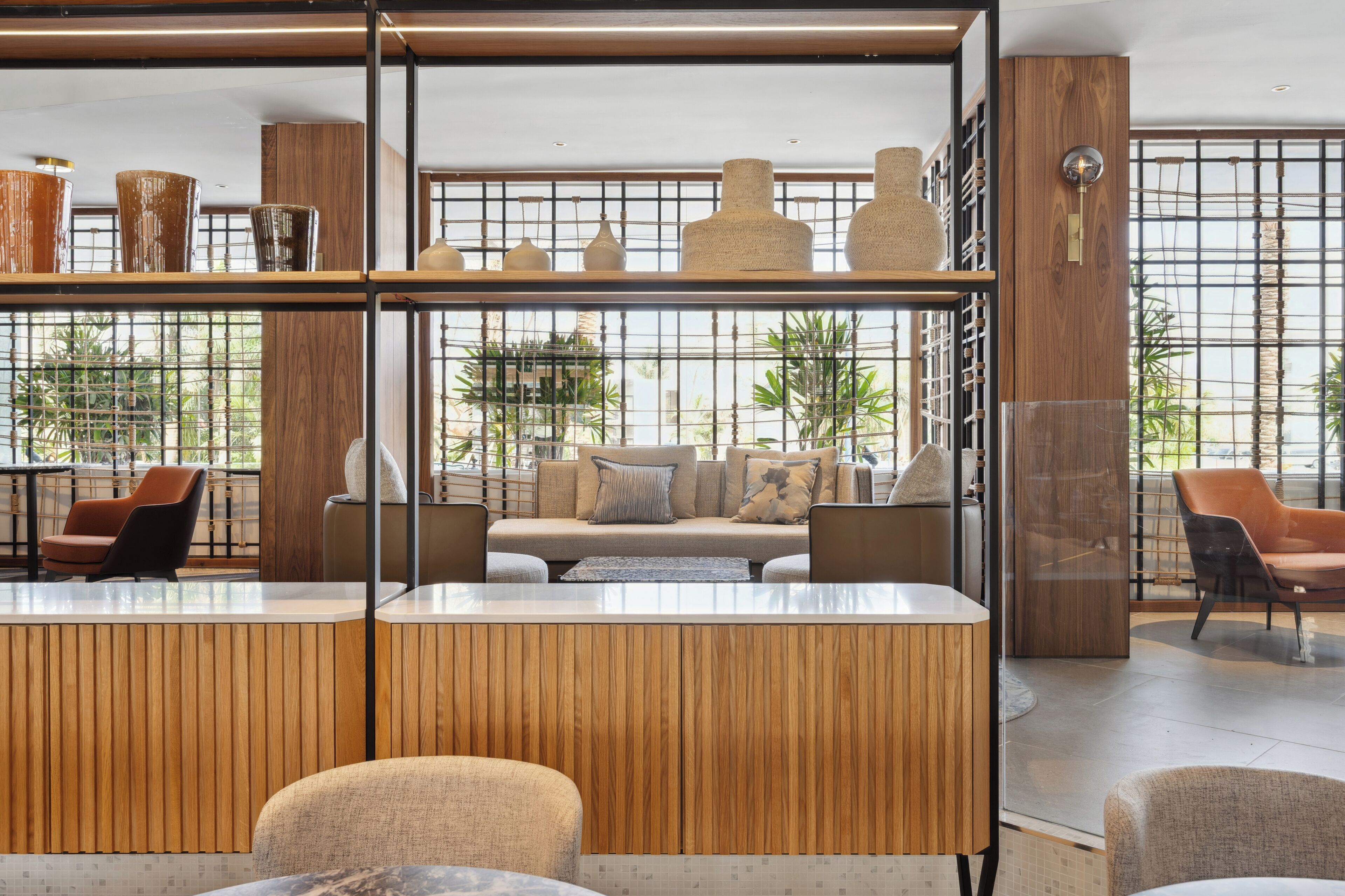 Un interior moderno con mostrador de recepción de madera, zona de estar y ventanas amplias.