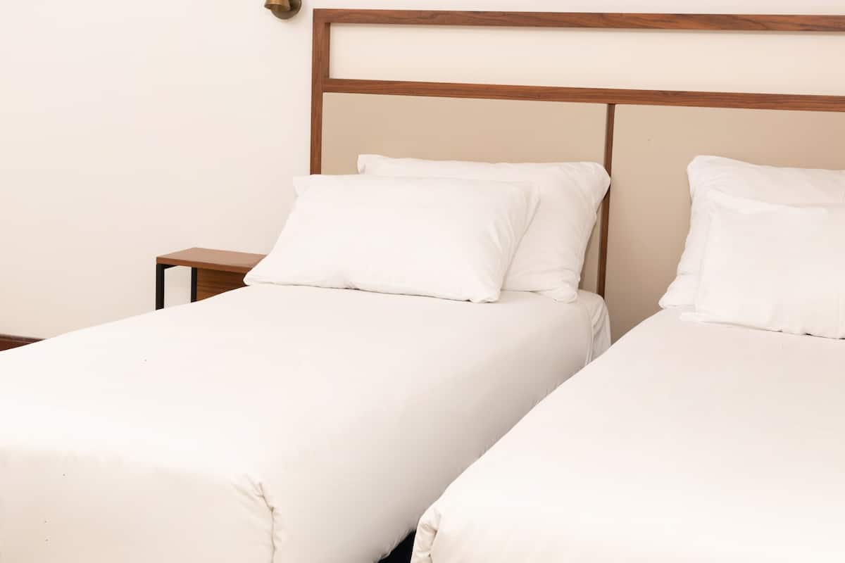 Duas camas de solteiro com cabeceiras de madeira e roupa de cama branca num quarto de hotel.
