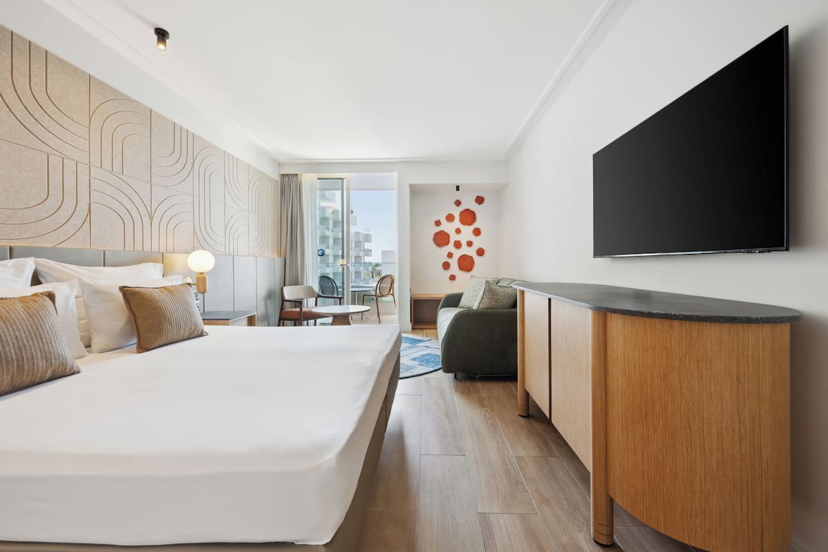 Quarto de hotel moderno com uma cama grande, uma escrivaninha, uma TV de tela plana e vista para a cidade.
