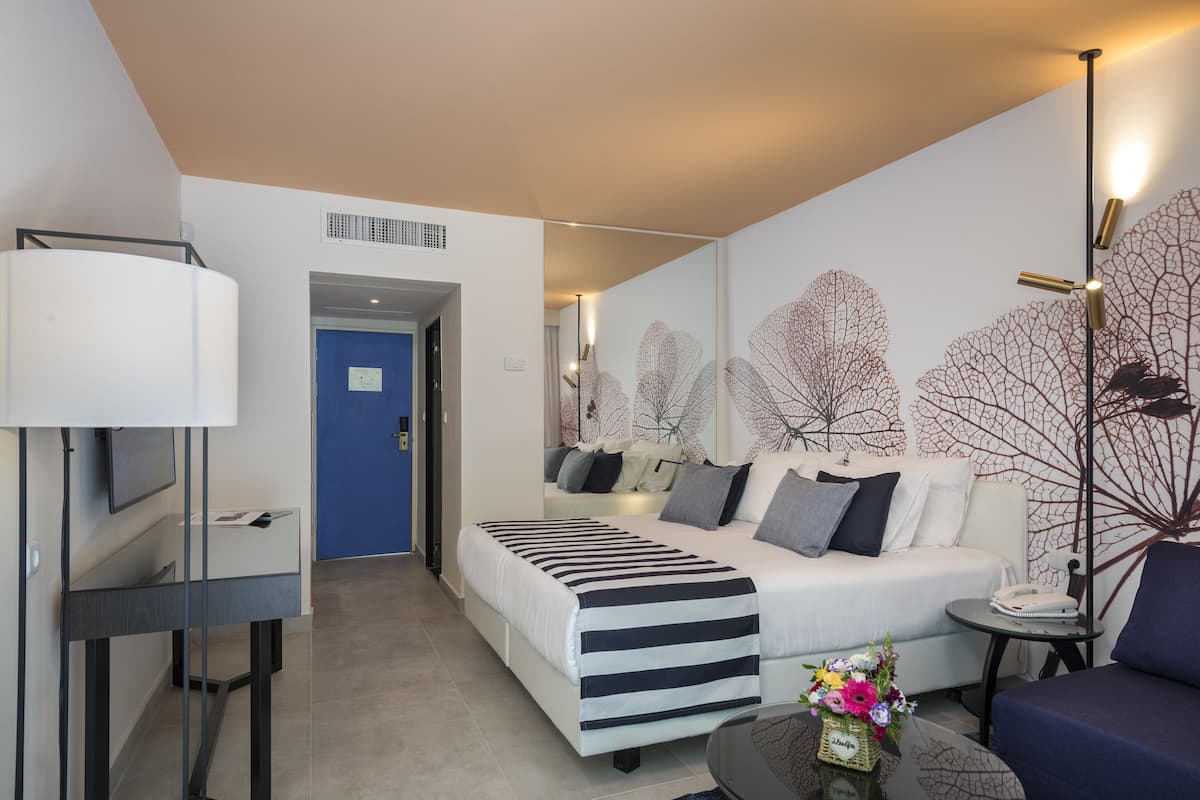 A modern hotel room with a bed, a desk, a chair, and a lamp.