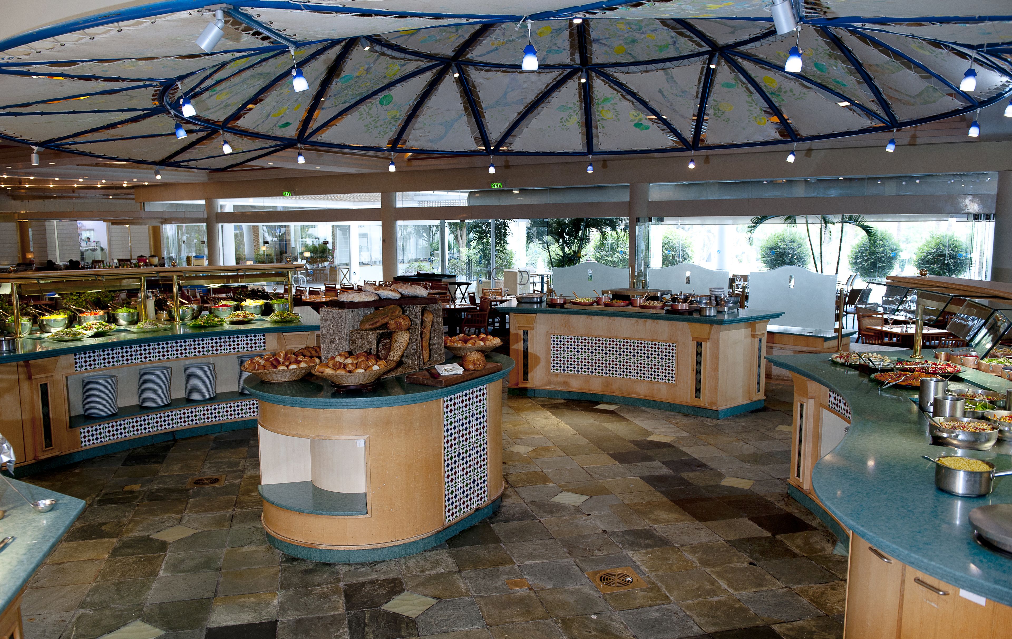 Ruime buffetruimte met diverse food stations, een centraal bedieningspunt en een plafond met een geometrisch patroon.
