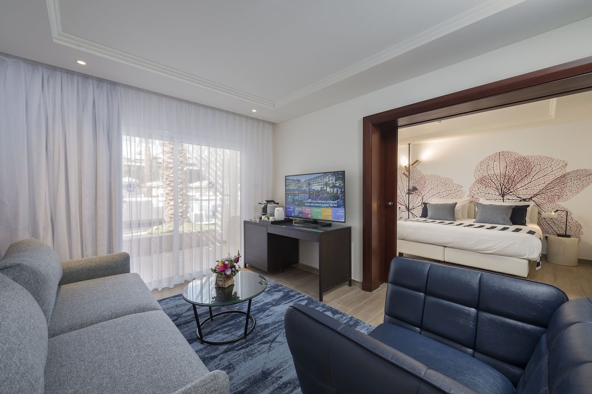 A modern hotel room with a sofa, a coffee table, a TV, and a bed with a unique leaf-patterned headboard.