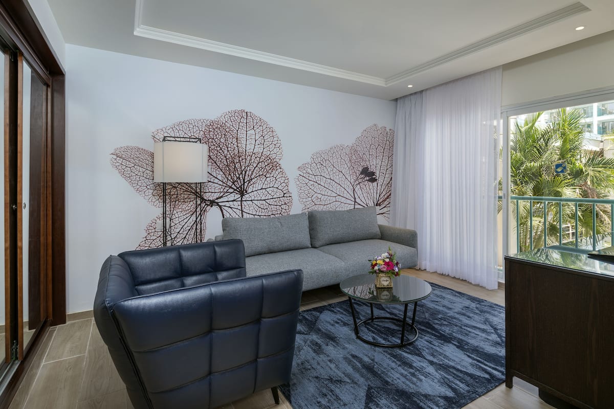A modern living room with a grey sofa, a black leather chair, a round coffee table with a vase of flowers, and a decorative wall with leaf patterns.