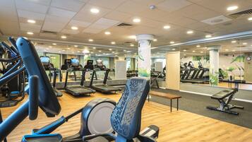 A gym with various exercise equipment, including treadmills and elliptical machines, arranged on a wooden floor.