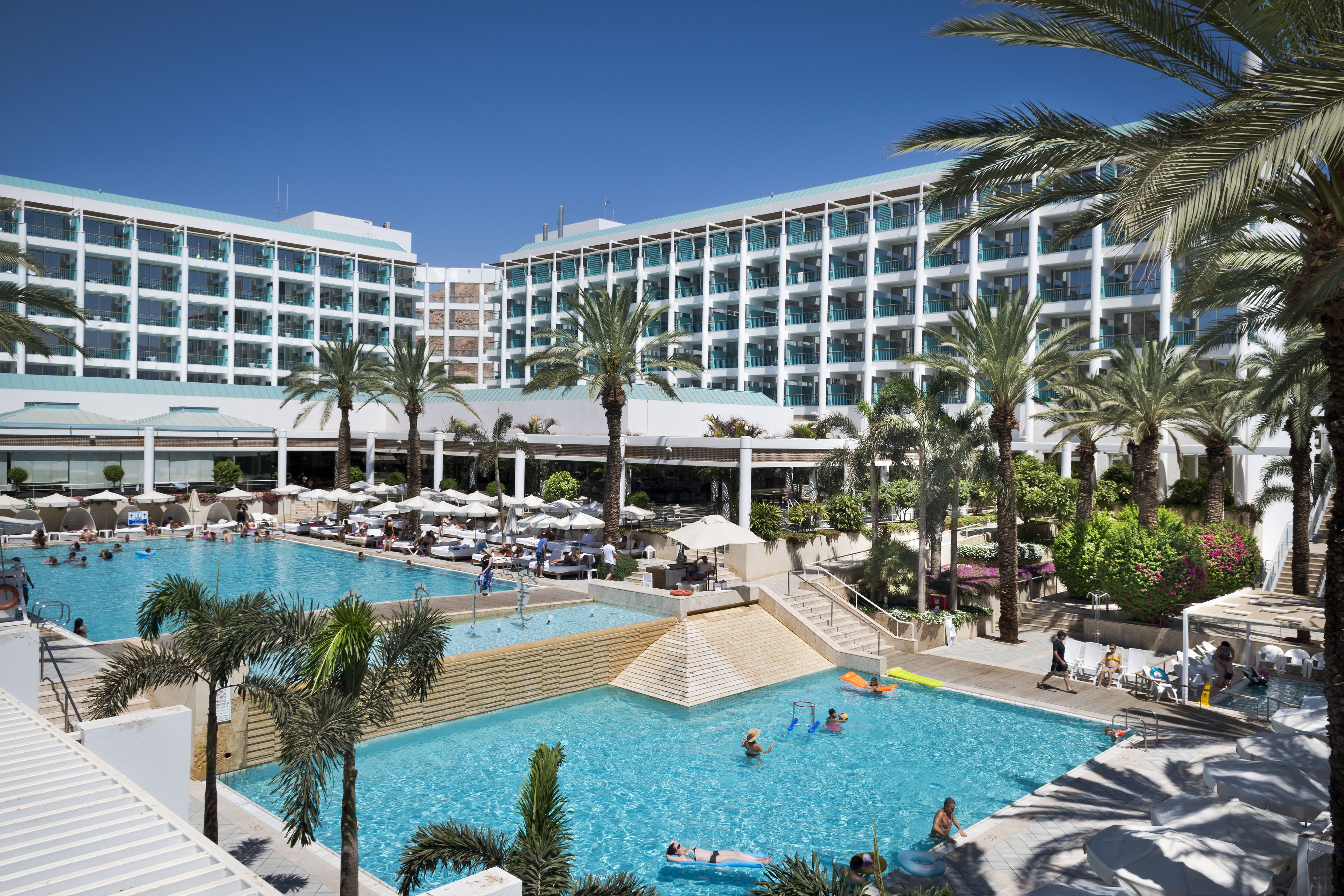 A hotel with a large pool area, multiple balconies, and palm trees.