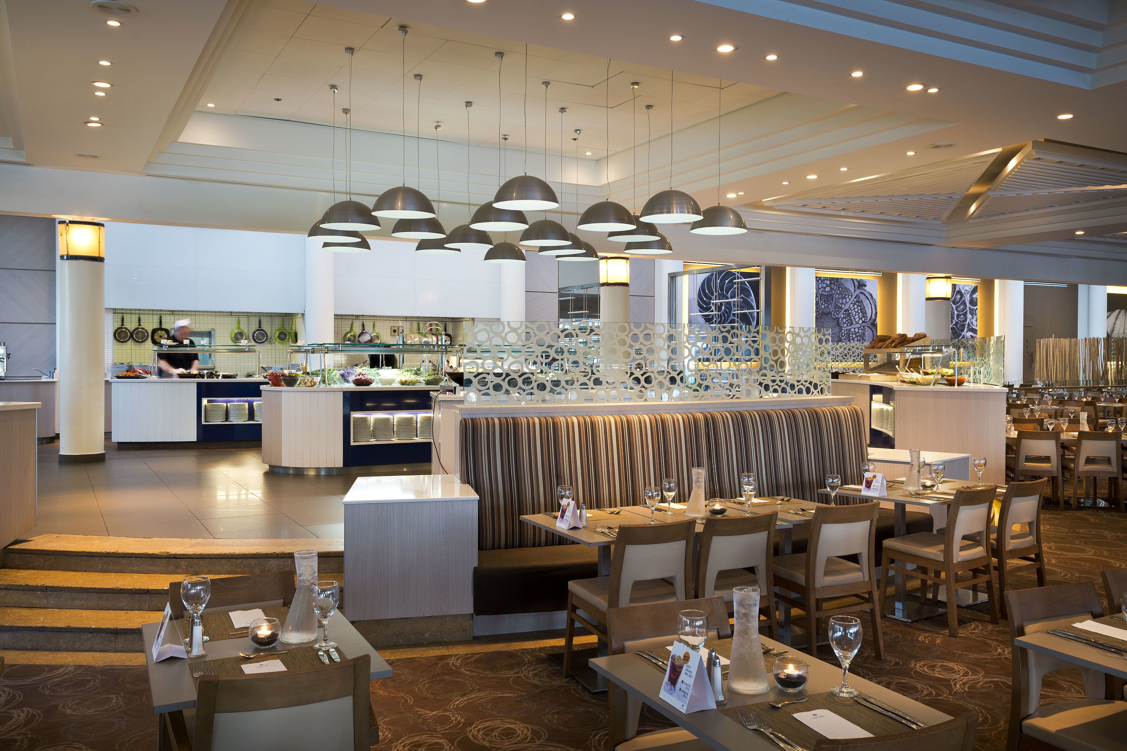 A modern restaurant with multiple dining areas, a bar, and a kitchen visible in the background.
