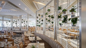 A modern restaurant with high ceilings, ample seating, and numerous potted plants on shelves. - Yam Suf by Isrotel Collection (Eilat)