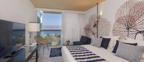 A modern hotel room with a large bed, a flat-screen TV, a desk with a chair, and a balcony with a view.