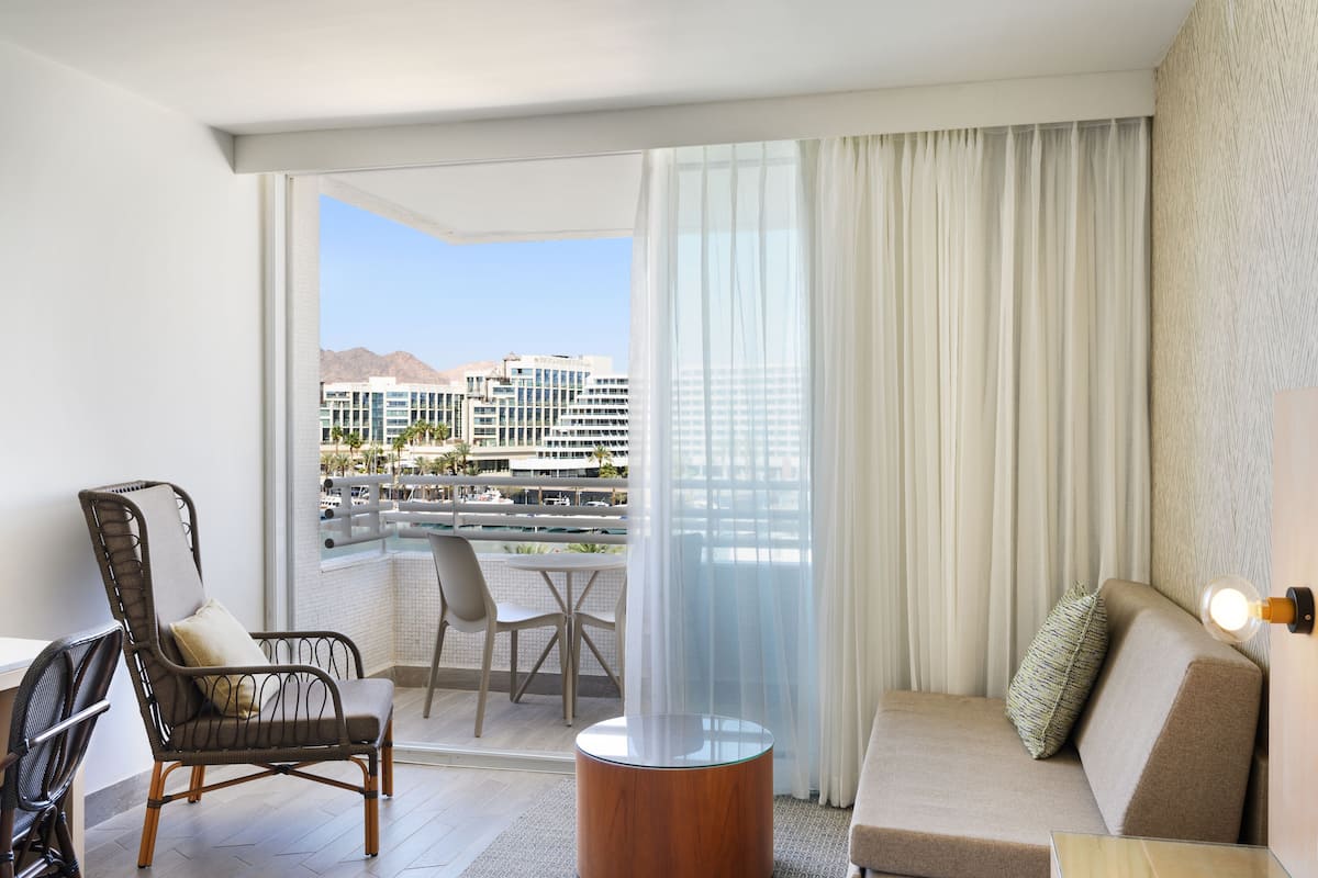 A modern hotel room with a balcony, a sofa, a chair, and a table.