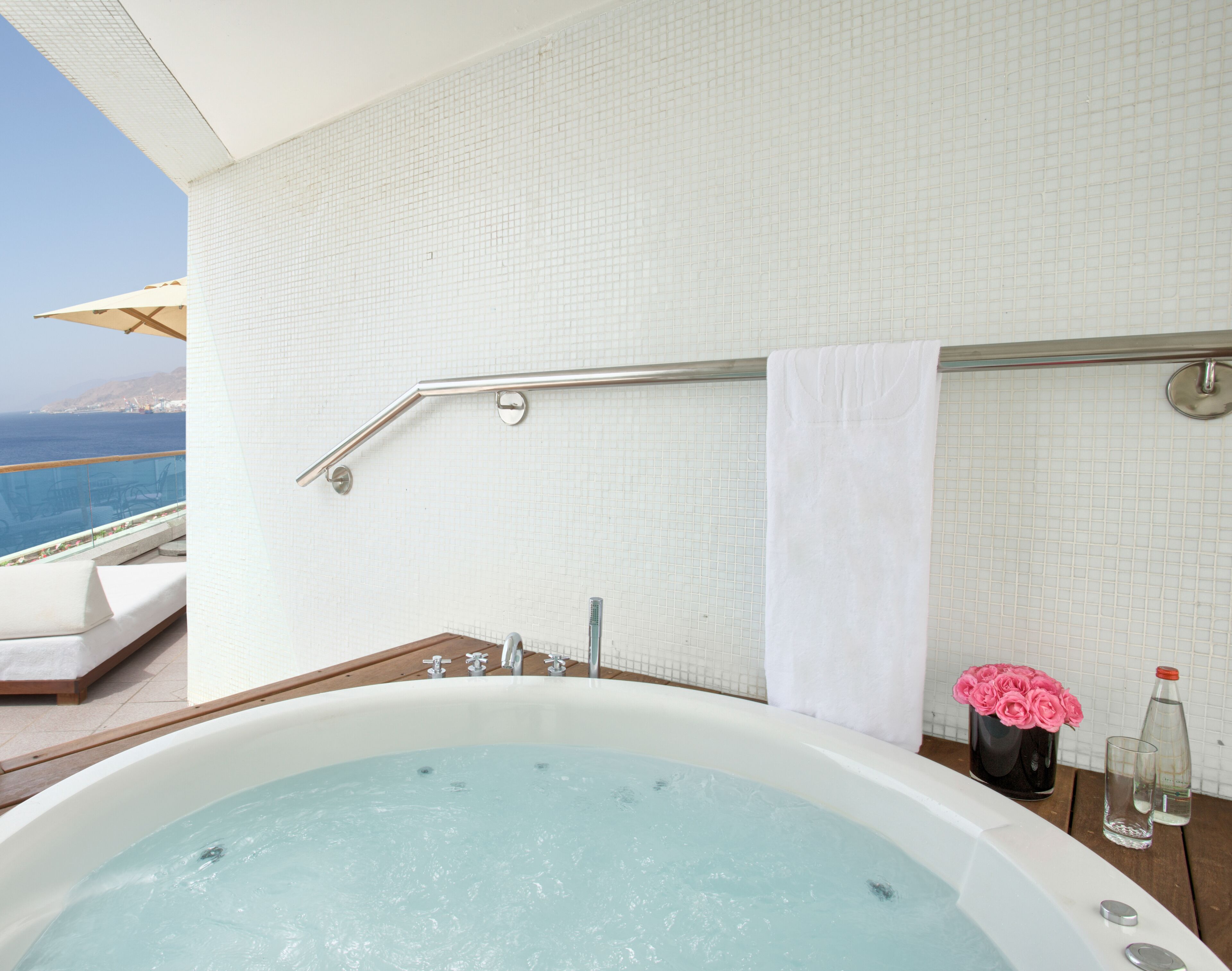 A bathroom with a bathtub, a towel rack, and a view of the ocean.