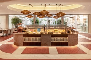 A breakfast bar with a variety of food items, a seating area with chairs, and a view of the outside through large windows.