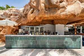 A bar area with a stone backdrop, a tiled counter, and a variety of bottles and glasses. - Royal Beach Eilat by Isrotel exclusive (Eilat)