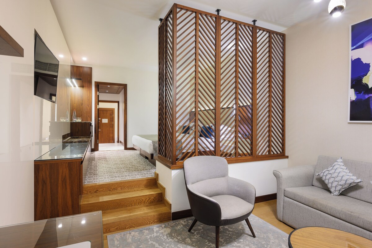 A modern living room with a sofa, a chair, a coffee table, a TV, and a wooden partition with a geometric pattern.