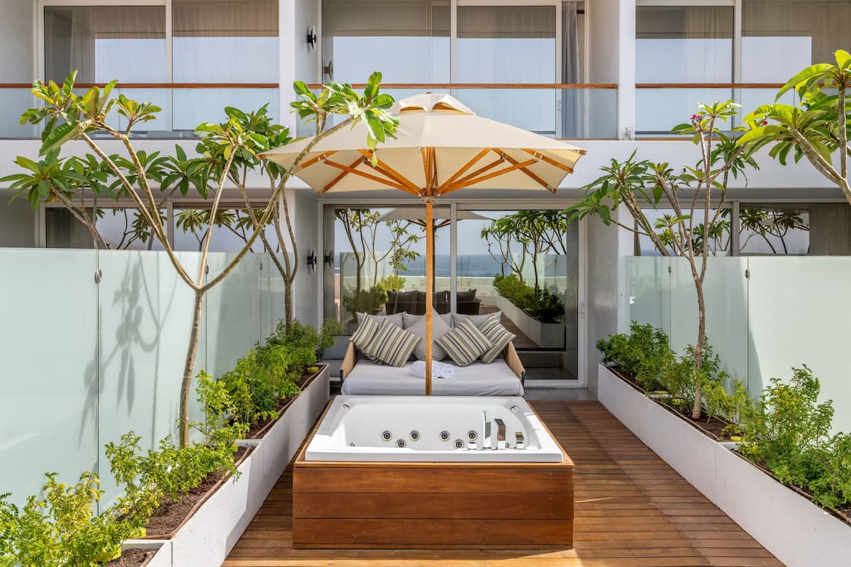 Un espace extérieur moderne, aménagé pour se détendre, avec une terrasse en bois, un jacuzzi intégré et un grand parasol pour créer de l’ombre.
