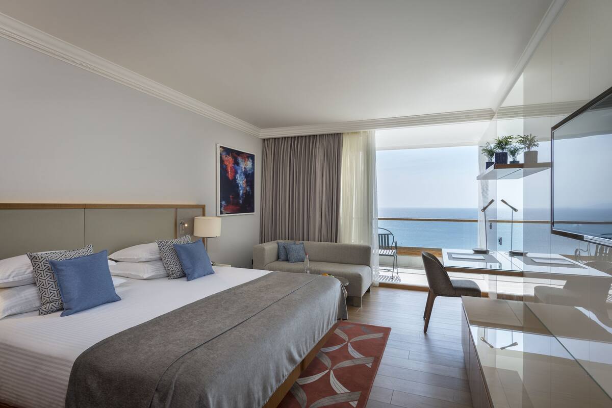Une chambre d’hôtel moderne dotée d’un grand lit, d’un canapé, d’un bureau et d’un balcon offrant une vue sur la mer.