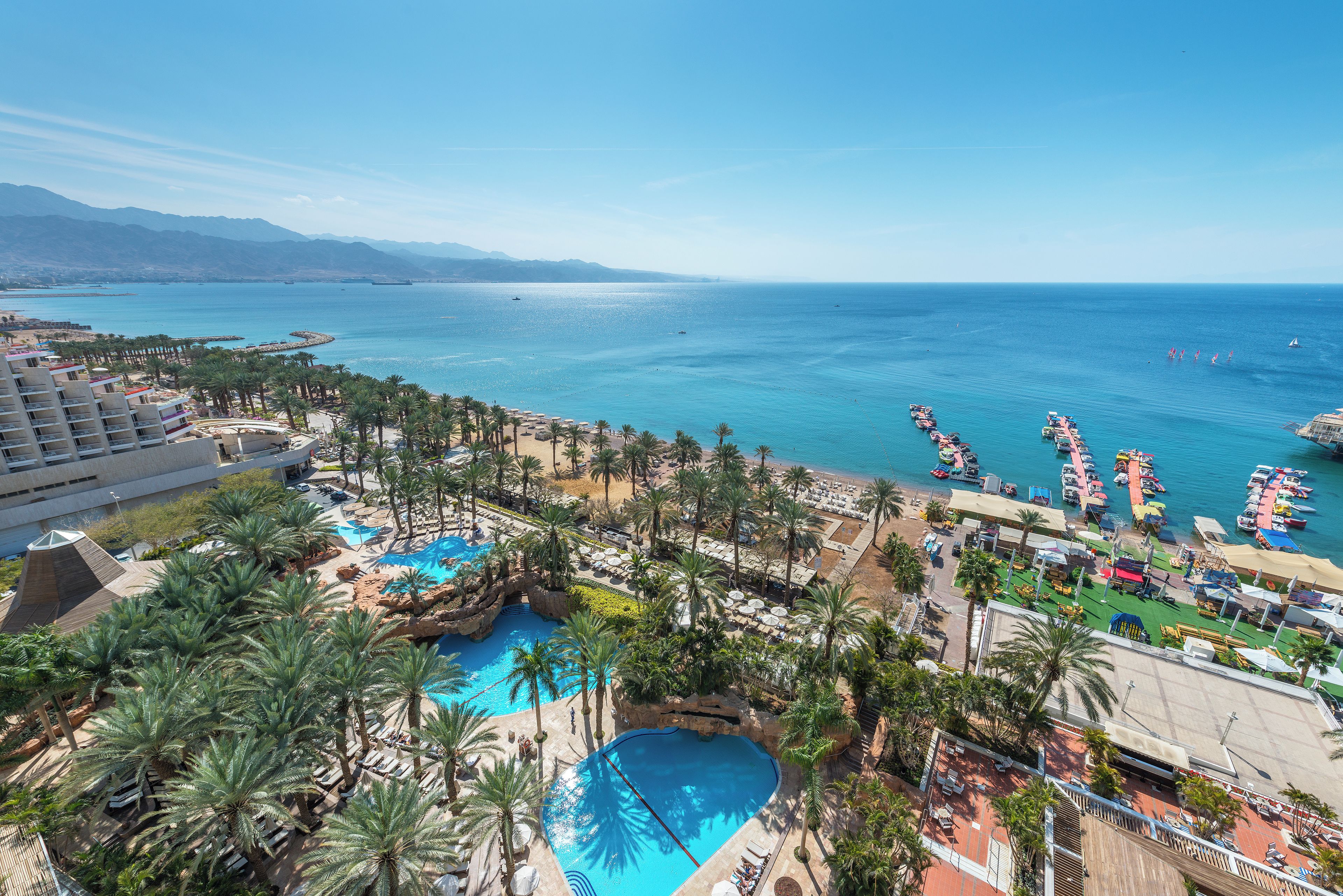 A resort with a large pool, palm trees, and a view of the sea.