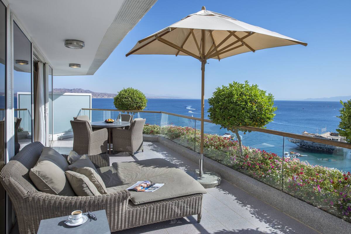 Un balcon agrémenté de meubles en osier, une table avec une tasse, et une vue sur la mer.