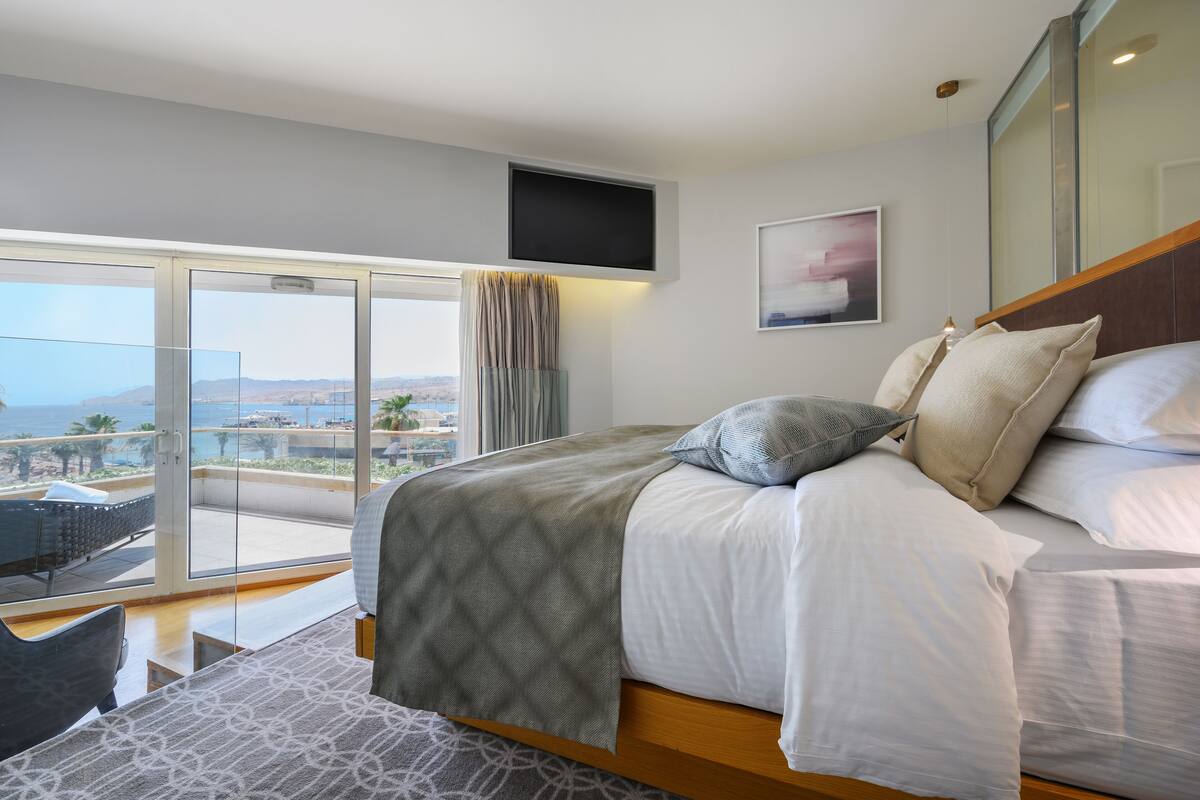 Une chambre moderne avec un grand lit, un téléviseur fixé au mur et un balcon offrant une vue sur la mer.