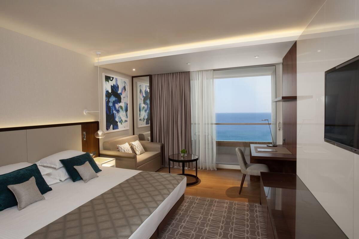 Une chambre d’hôtel moderne, dotée d’un grand lit, d’un bureau, d’une chaise et offrant une vue sur la mer.