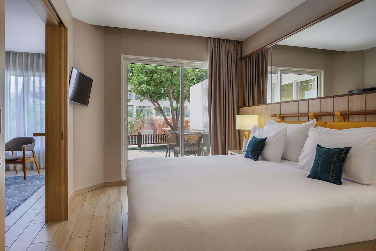 A hotel room with a large bed, a TV mounted on the wall, a desk with a chair, and a view of the outdoors.